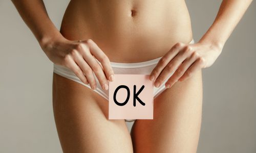 Woman health. Female model holding card near stomach. Young adult girl with paper with OK sign or symbol isolated on gray studio background. Cut out part of body. Medical problem and solution.